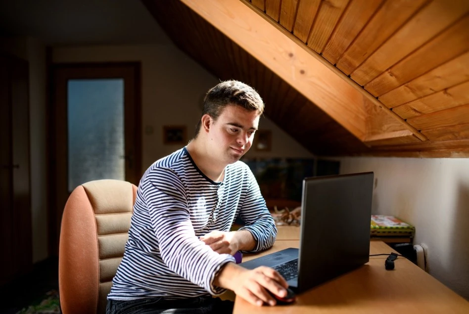 Boy with down syndrome sitting at desk using laptop