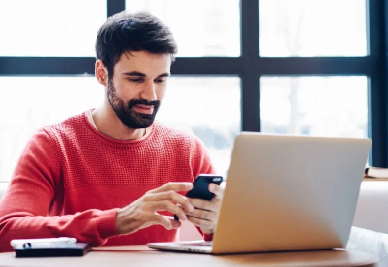 Man sitting at desk with laptop and using phone